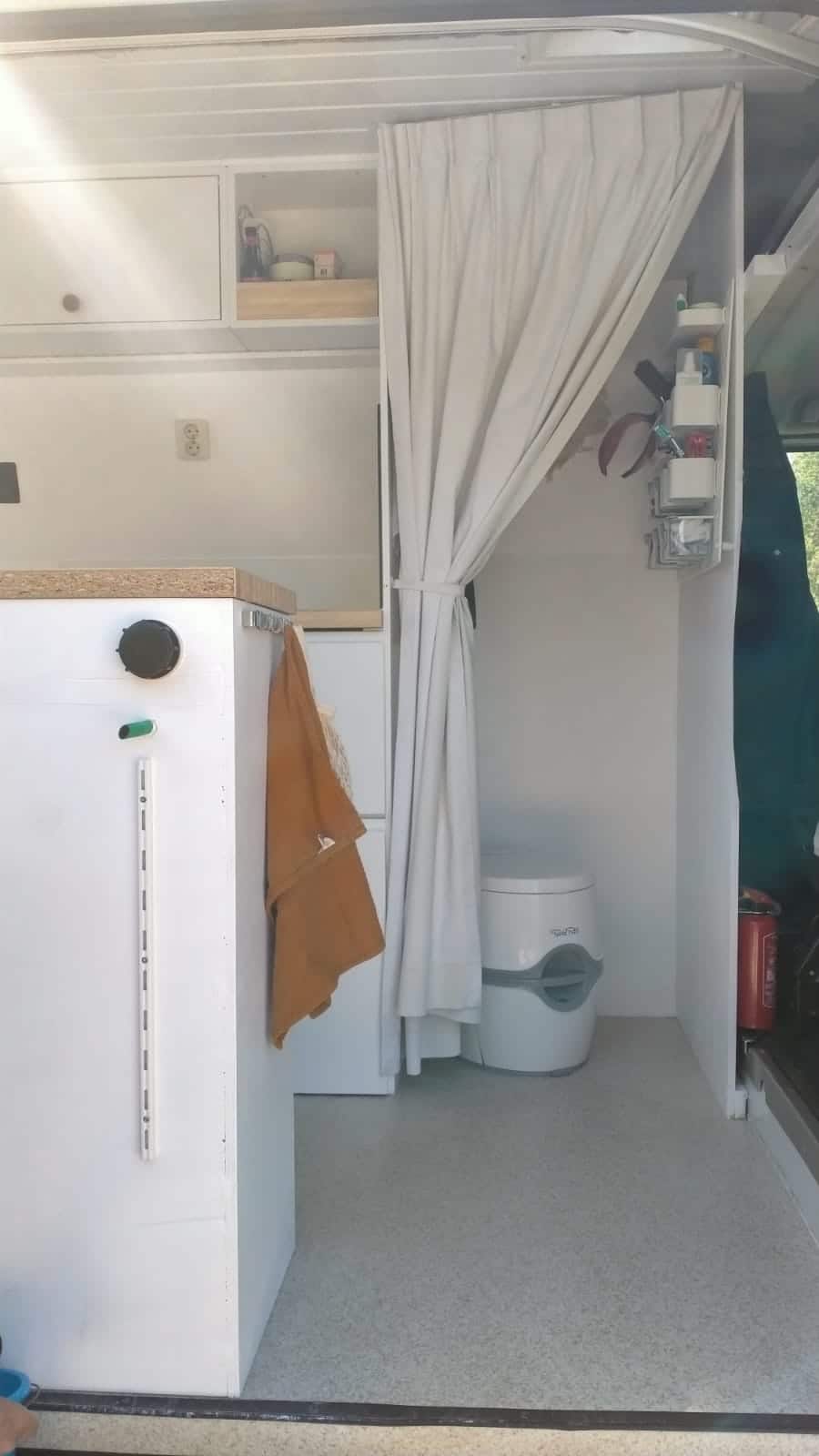 Toilet, en væg med toiletartikler, et spejl og et tørrestativ i autocamperen.